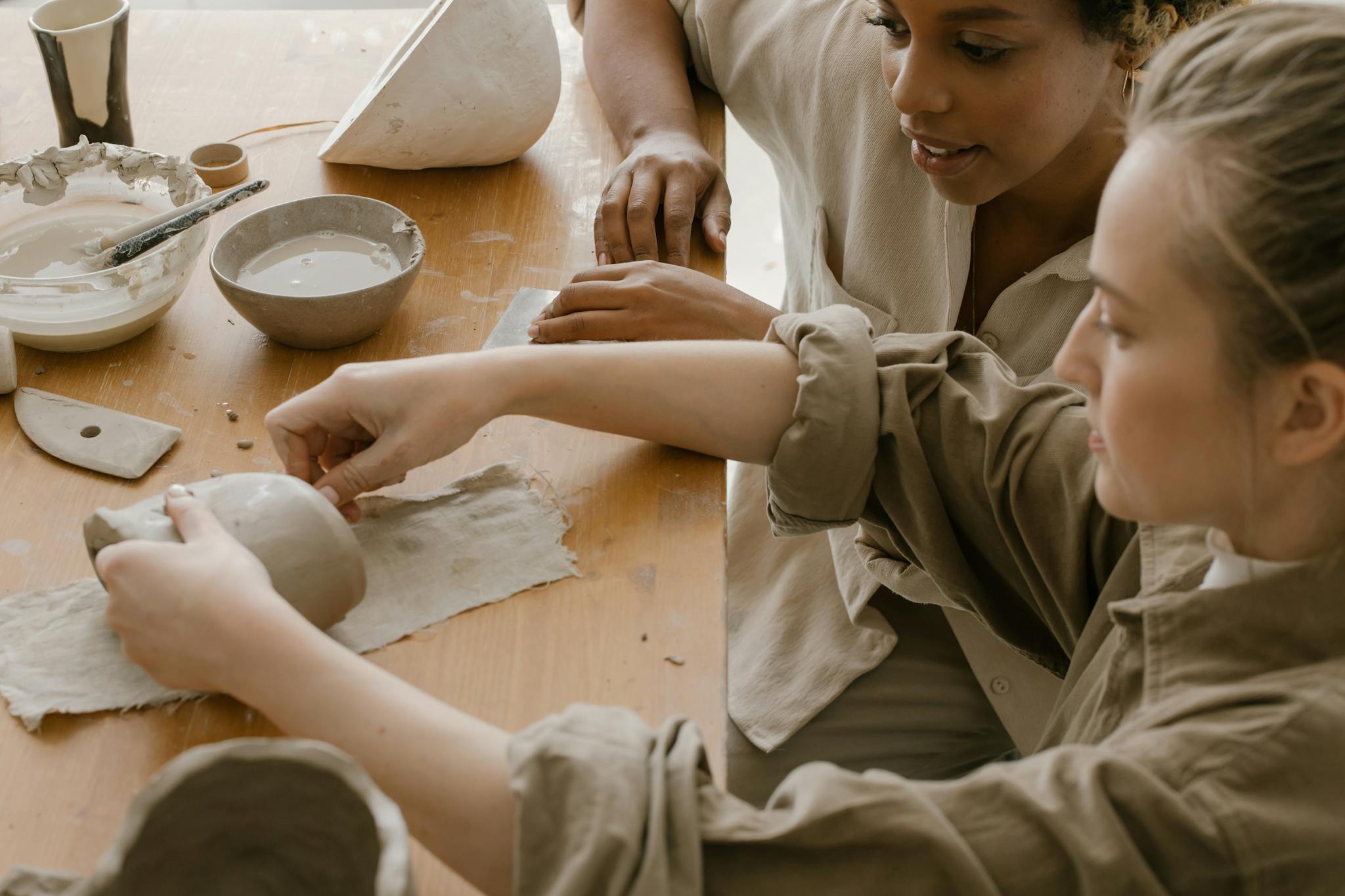 Two women engaging in pottery crafting with clay and tools on a tabletop.