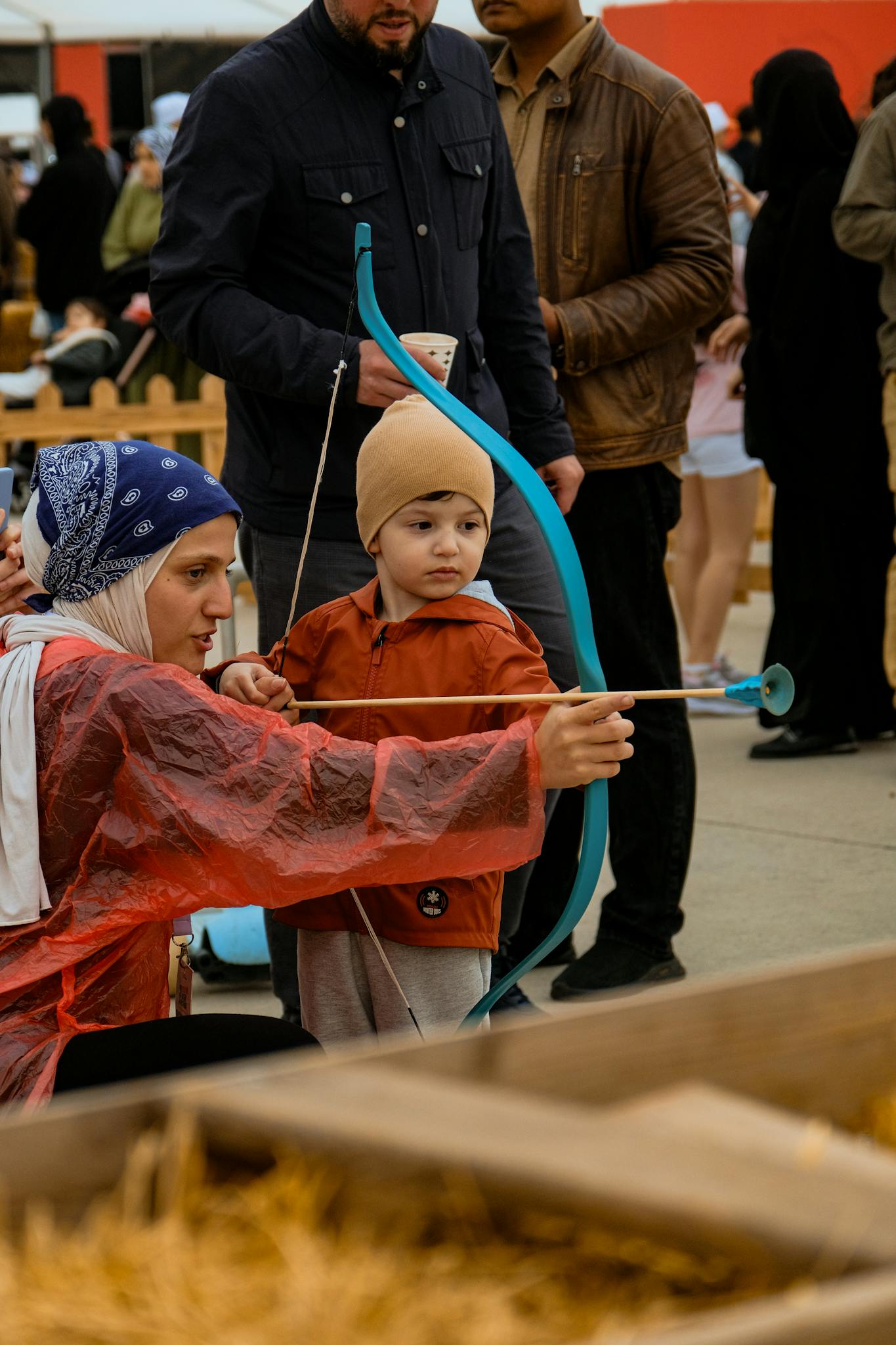 Young child learning archery with an instructor at an outdoor event.